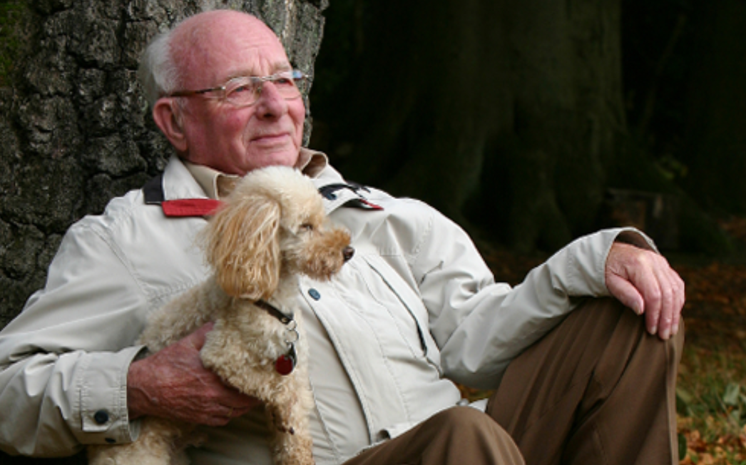 An older man sitting next to a tree with a dog.